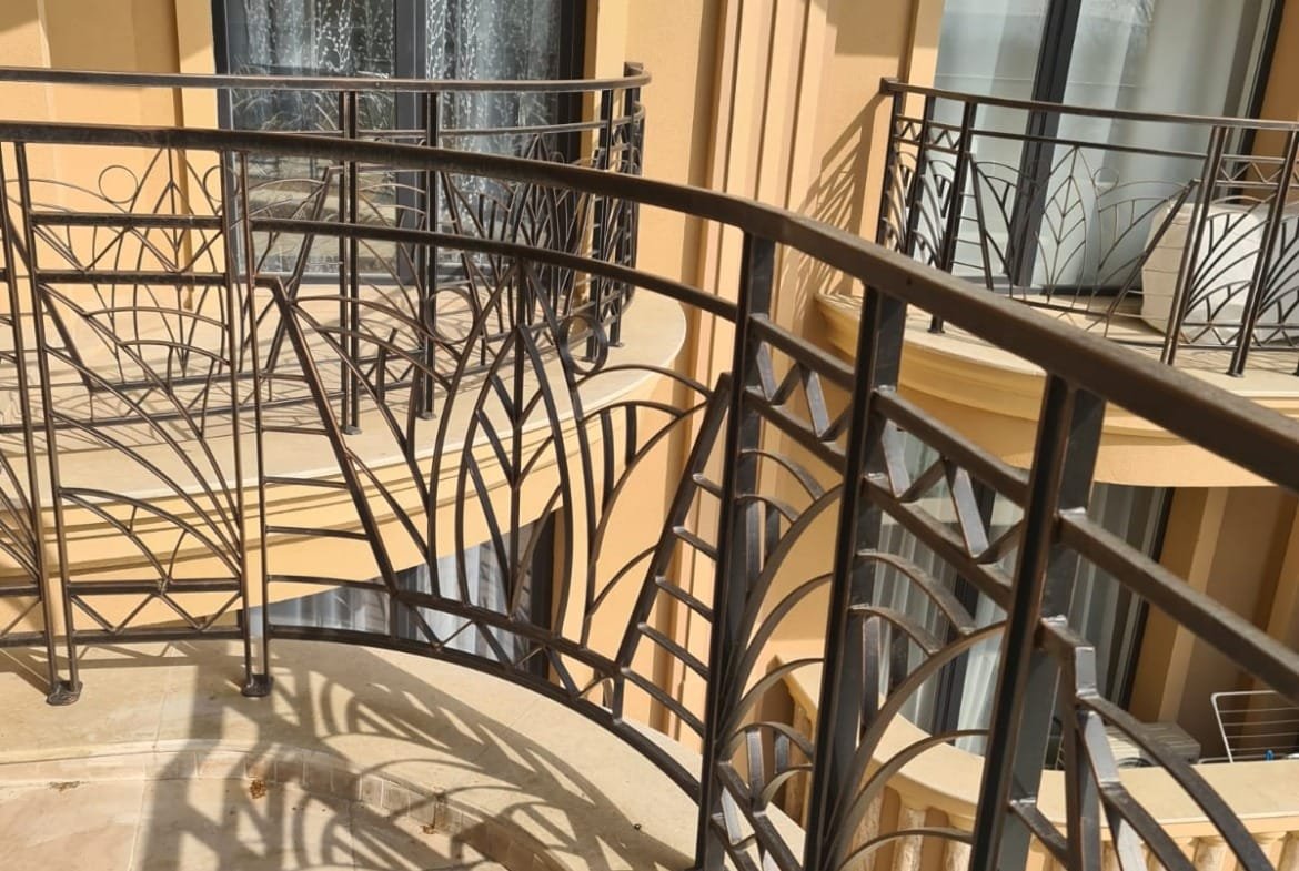 Балкон с кованым ограждением и вид на окна, отражающие стиль жилья в Болгарии для покупателей недвижимости.