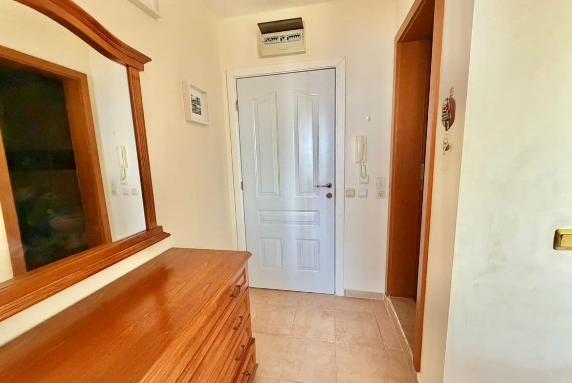 Светлый коридор с деревянным комодом, зеркалом и дверью, создающий уютную атмосферу для покупателей недвижимости в Болгарии.