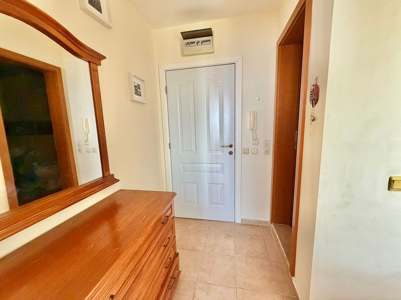 Светлый коридор с деревянным комодом, зеркалом и дверью, создающий уютную атмосферу для покупателей недвижимости в Болгарии.