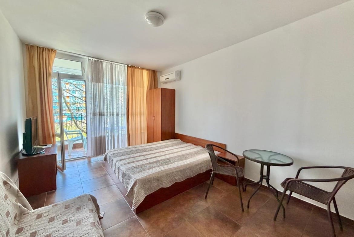 Светлая квартира с двуспальной кроватью, телевизором, столом и стульями, выход на балкон с видом на природу. Купить недвижимость в Болгарии.