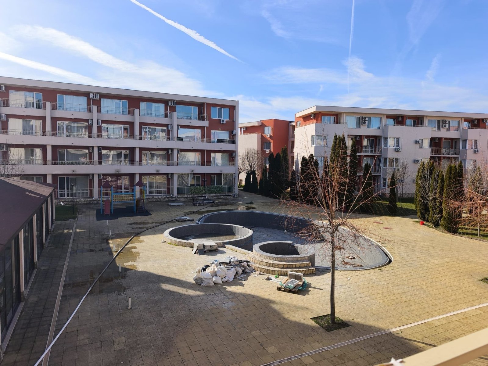 Двор жилого комплекса с площадкой и строительными материалами Жилой комплекс в Болгарии с площадкой для отдыха, свежим воздухом и зелеными насаждениями, подходящий для покупки недвижимости.