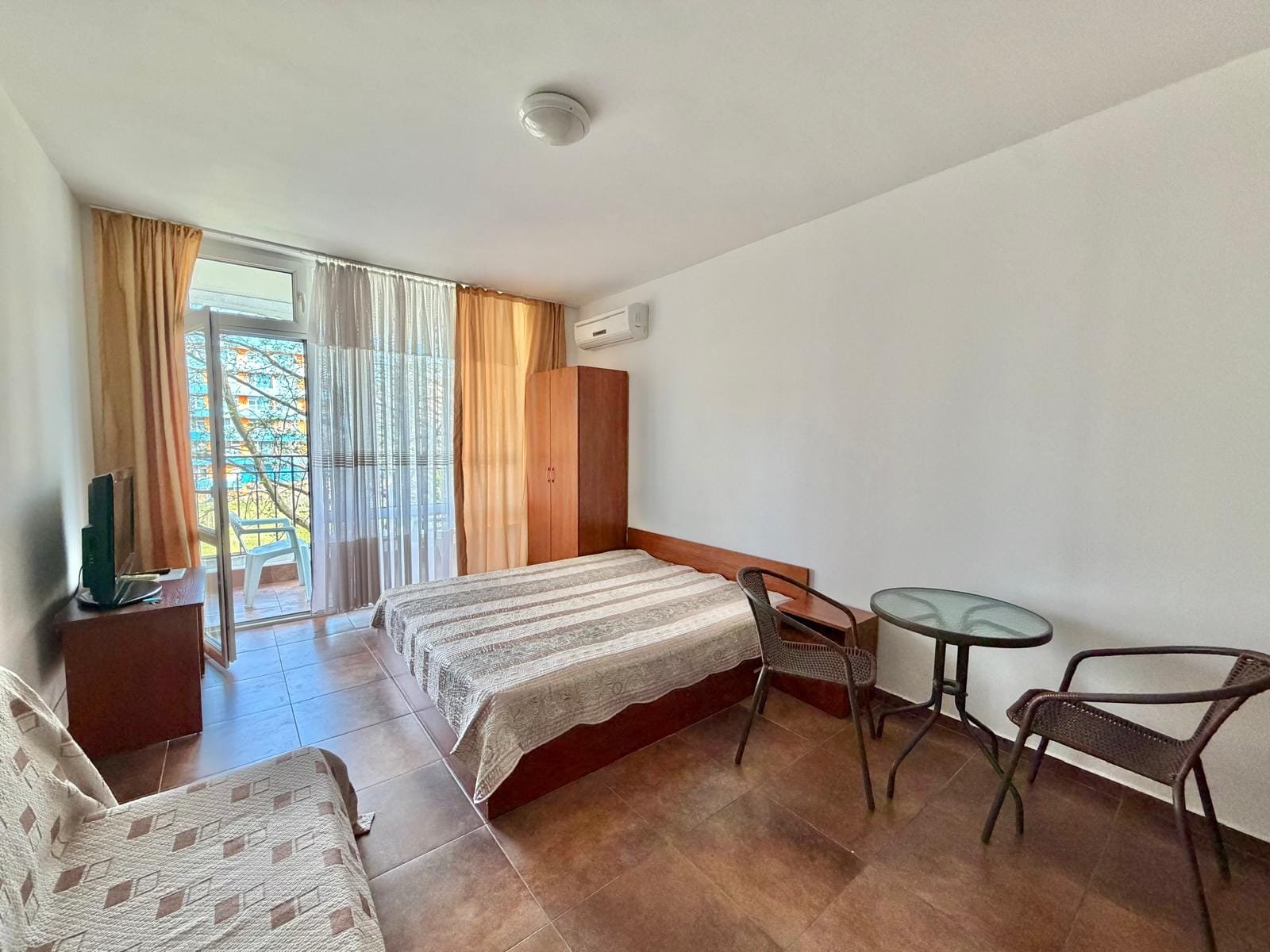 Светлая квартира с двуспальной кроватью, телевизором, столом и стульями, выход на балкон с видом на природу. Купить недвижимость в Болгарии.