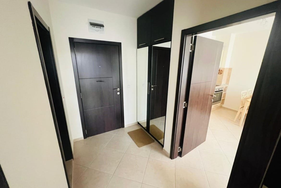 Современный коридор квартиры в Болгарии с темными дверями, зеркалом и плиточным полом, готовый для продажи.