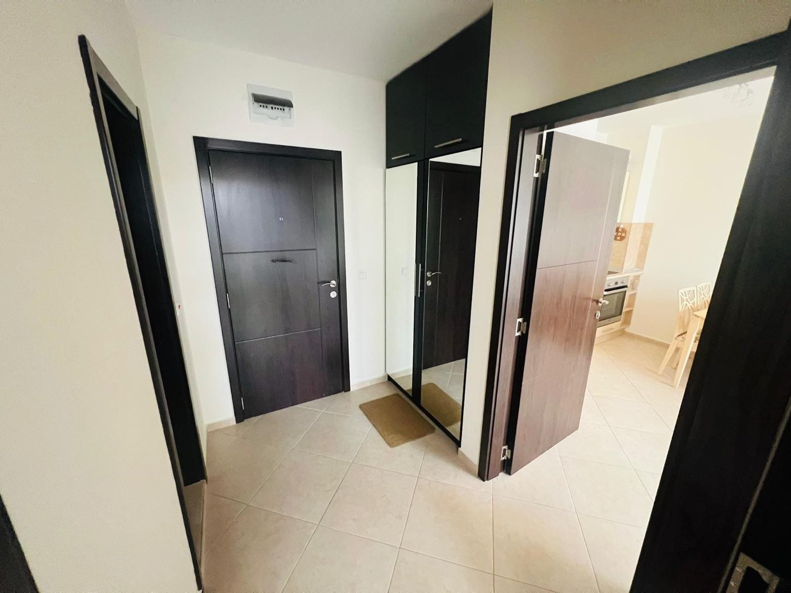 Современный коридор квартиры в Болгарии с темными дверями, зеркалом и плиточным полом, готовый для продажи.