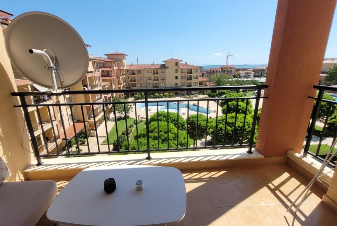 Балкон с видом на бассейн и зеленый двор, идеальное место для отдыха в жилом комплексе в Болгарии.