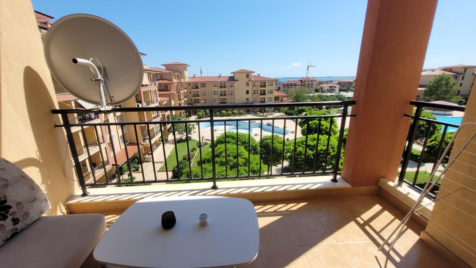 Балкон с видом на бассейн и зеленый двор, идеальное место для отдыха в жилом комплексе в Болгарии.