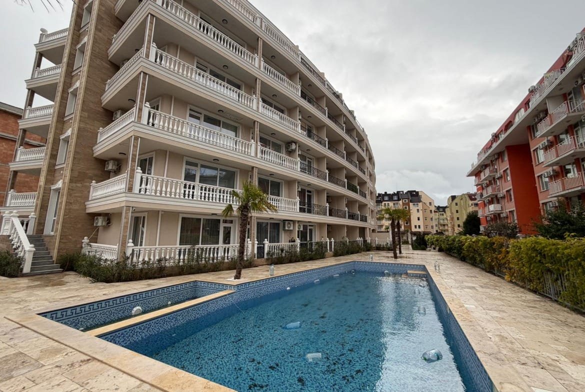 Современный жилой комплекс с отделкой и бассейном на фоне облачного неба, идеальный для покупки недвижимости в Болгарии.