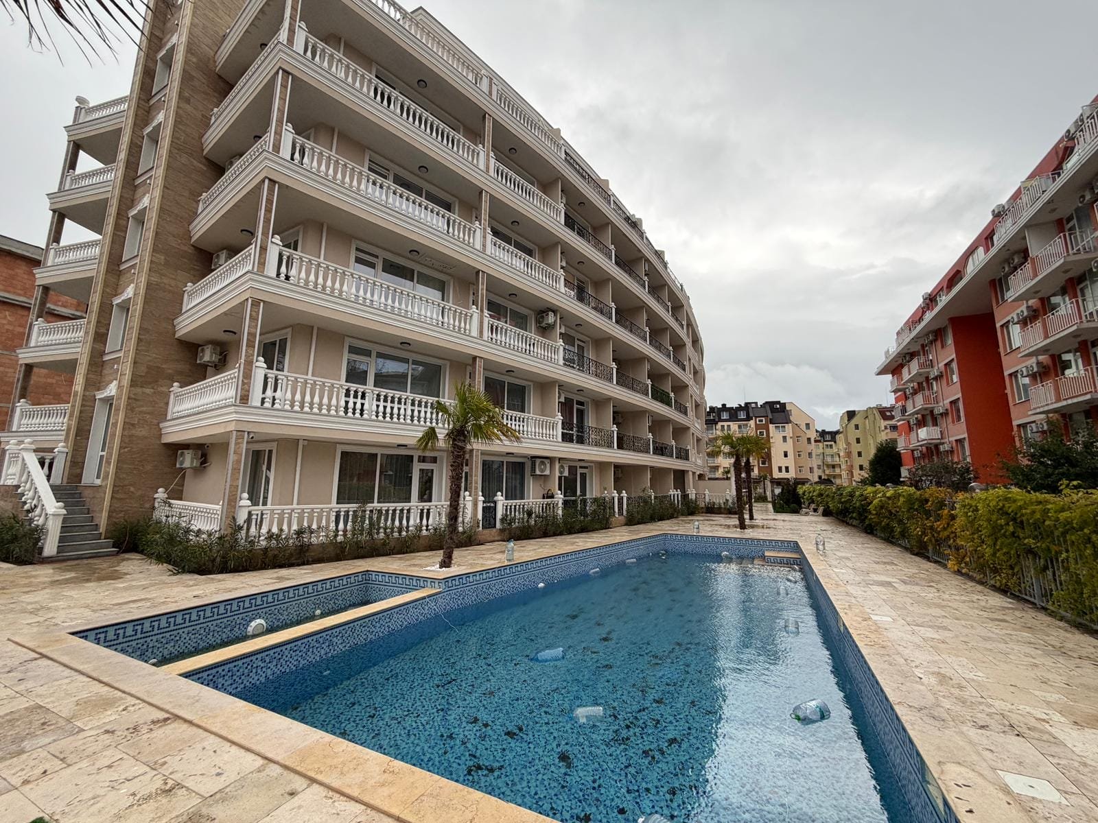 Современный жилой комплекс с отделкой и бассейном на фоне облачного неба, идеальный для покупки недвижимости в Болгарии.