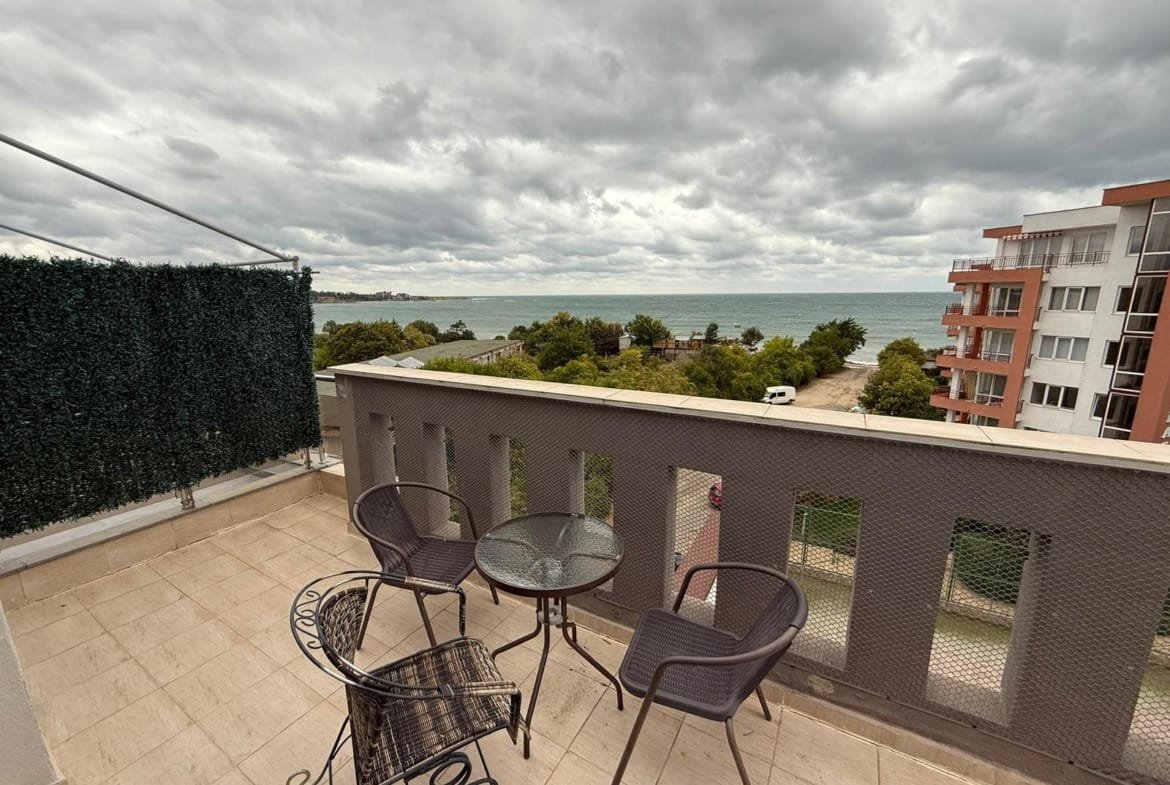 Балкон с пластиковыми столом и стульями, с видом на море и облачное небо в Болгарии. Идеальное место для отдыха.