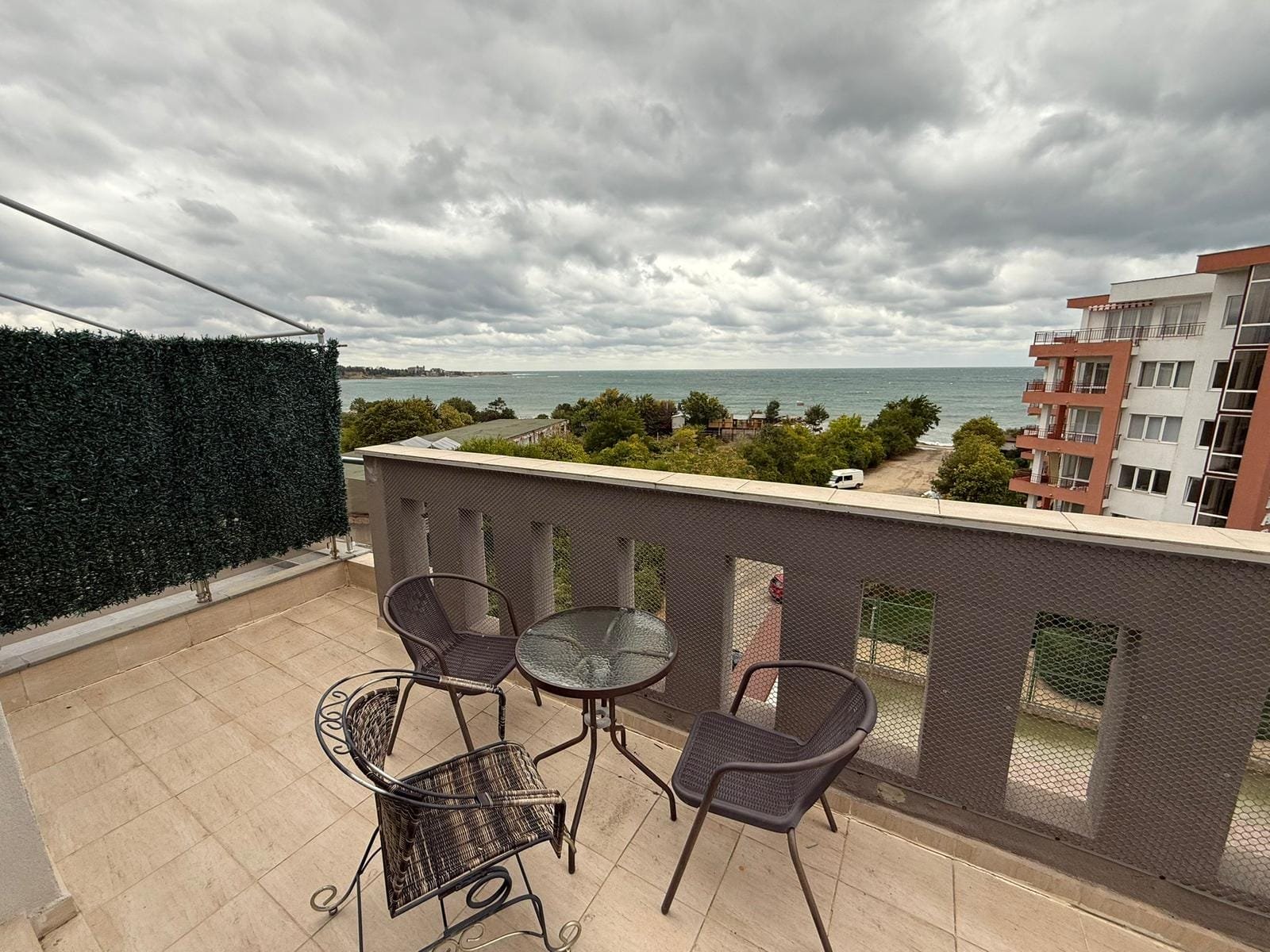 Балкон с пластиковыми столом и стульями, с видом на море и облачное небо в Болгарии. Идеальное место для отдыха.