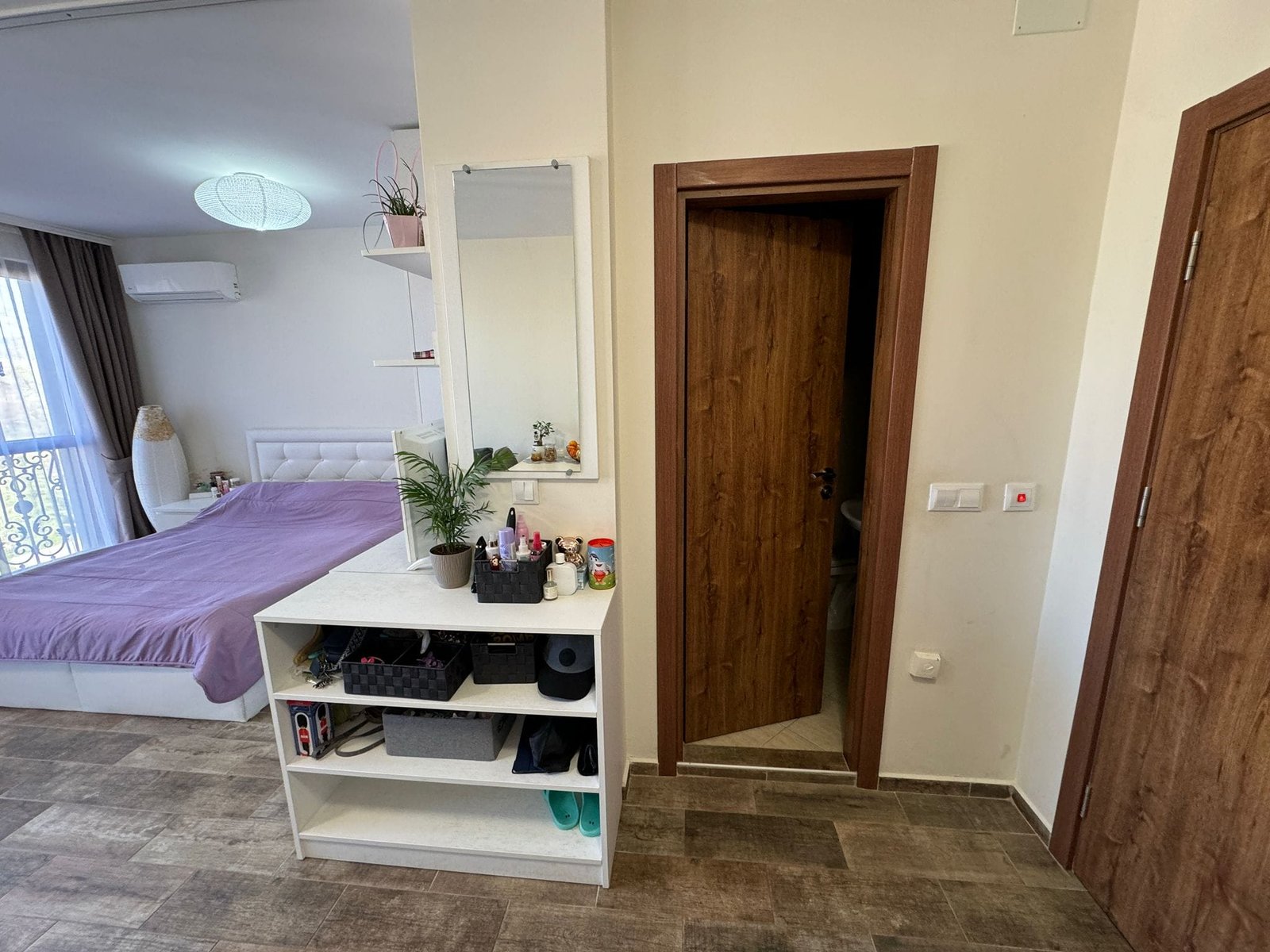 Современный интерьер квартиры: спальня и вход в ванную комнату Современная квартира в Болгарии, светлая спальня с балконом и стильной мебелью, дверь в ванную и просторный интерьер.