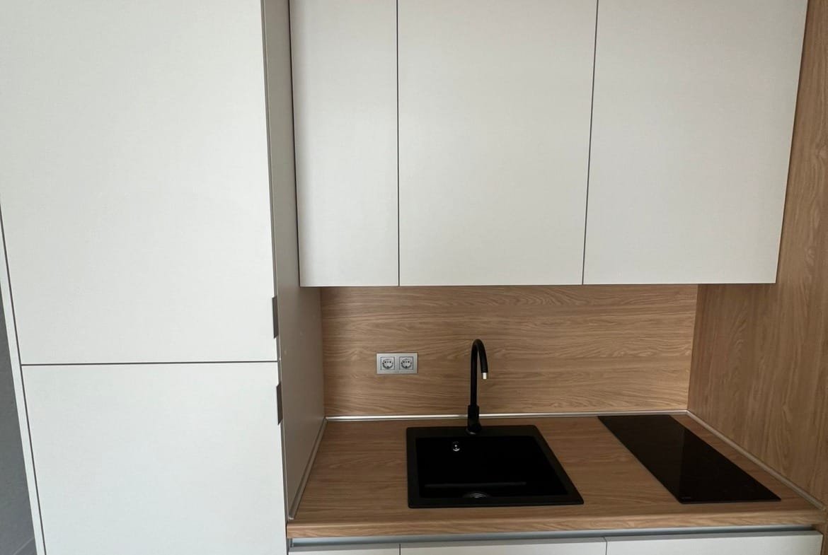 Современная кухня в стиле минимализм с белыми и деревянными фасадами, черной раковиной и варочной панелью в Болгарии.