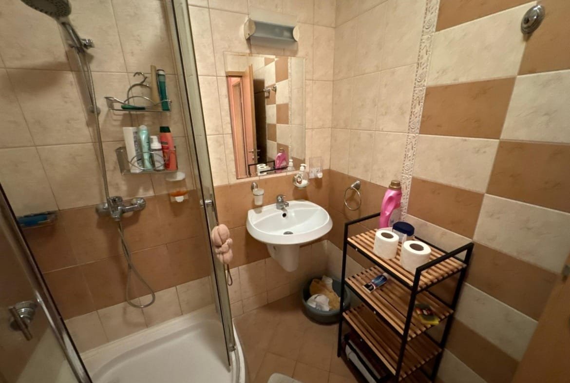 Современная ванная комната с душевой кабинкой, раковиной, полочками и туалетной бумагой, выполненная в светлых тонах.