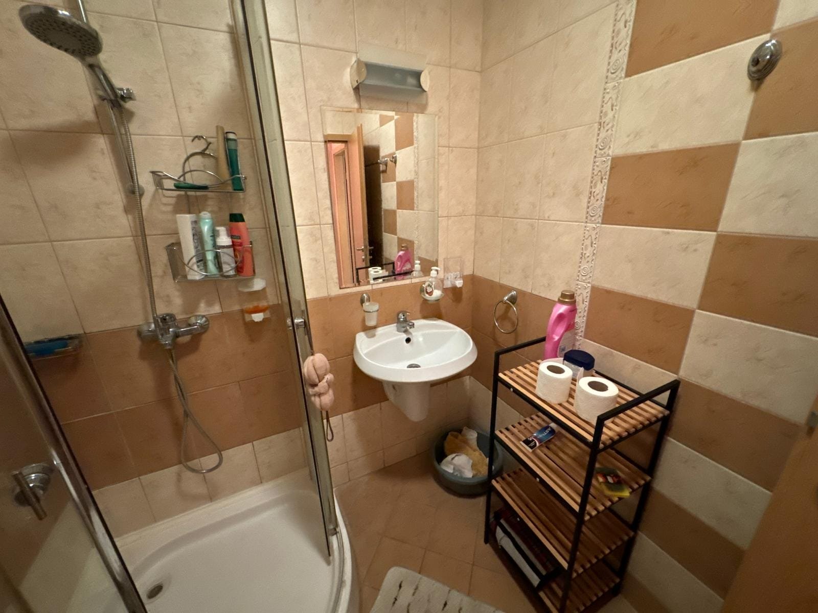 Современная ванная комната: душевая, раковина и полки для хранения Современная ванная комната с душевой кабинкой, раковиной, полочками и туалетной бумагой, выполненная в светлых тонах.