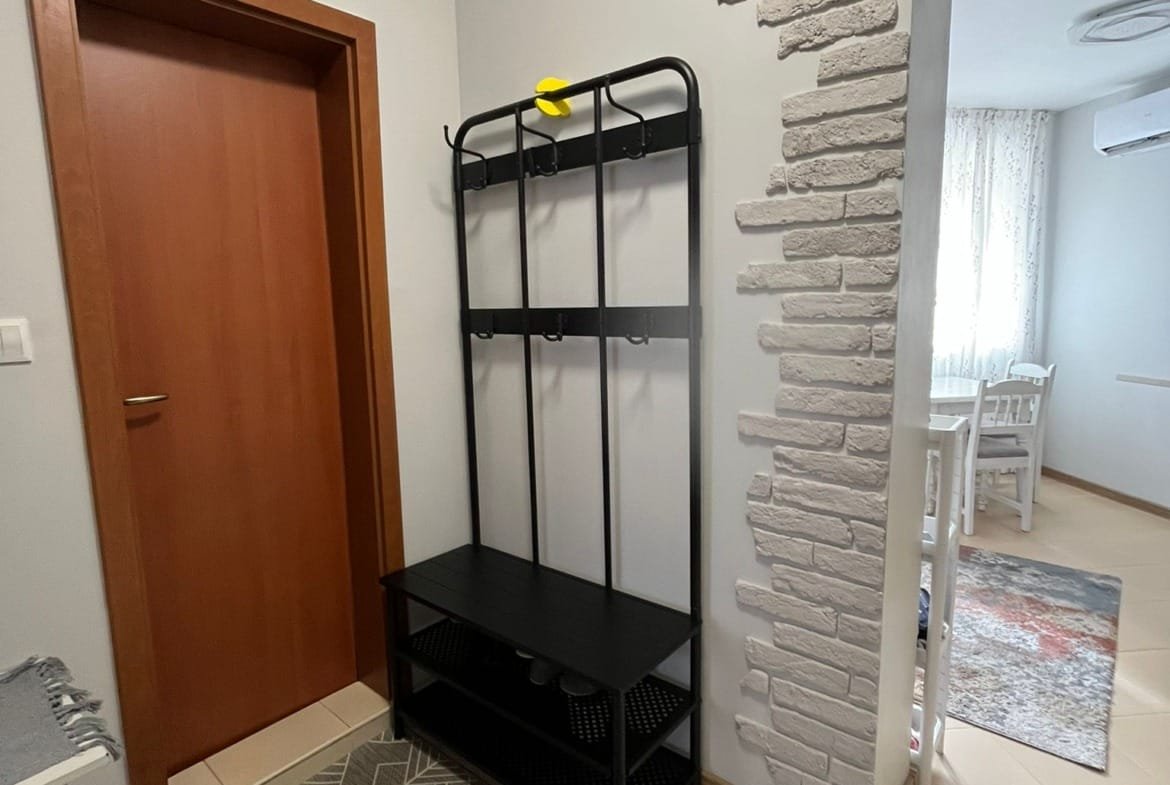 Прихожая с чёрной вешалкой для верхней одежды, светлыми стенами и плиточным полом, создающая уютную атмосферу.