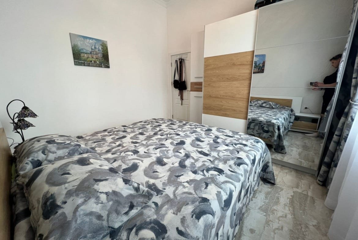 Современная спальня с двуспальной кроватью, зеркальным шкафом и светлыми стенами, идеальное место для отдыха в Болгарии.