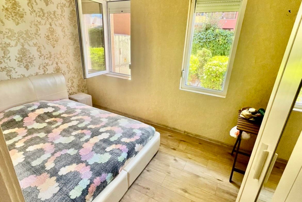 Современная спальня с белой кроватью, светлыми стенами и большими окнами, создающими уютную атмосферу для отдыха.