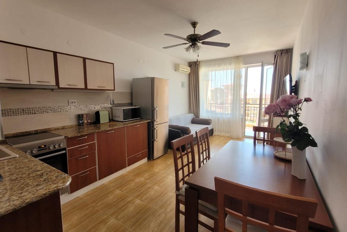 Современная кухня-студия с обеденным столом, холодильником и диваном, идеально подходящая для покупки недвижимости в Болгарии.