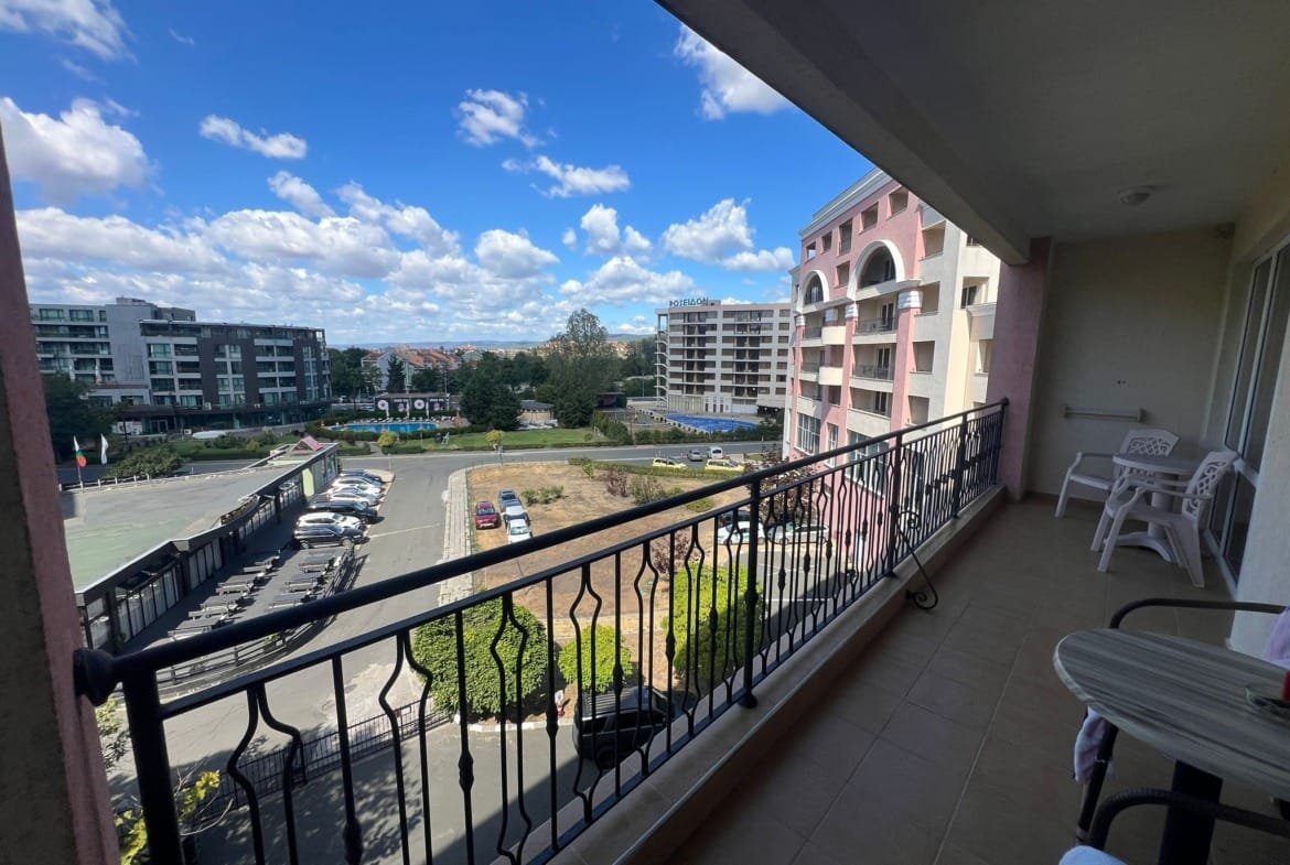 Балкон с видом на жилые комплексы в Болгарии, солнечное небо, зеленые насаждения и парковка. Идеально для покупки недвижимости.