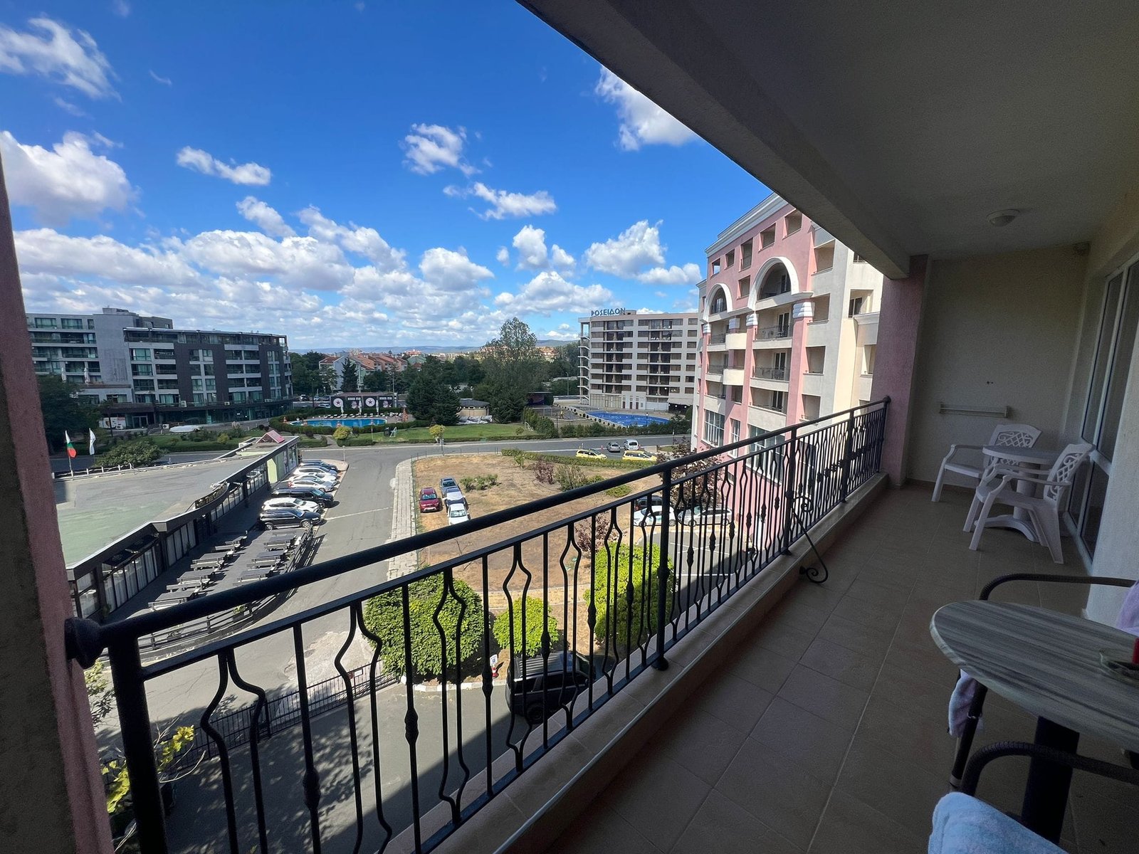 Красивая терраса с видом на городской ландшафт и облака Балкон с видом на жилые комплексы в Болгарии, солнечное небо, зеленые насаждения и парковка. Идеально для покупки недвижимости.