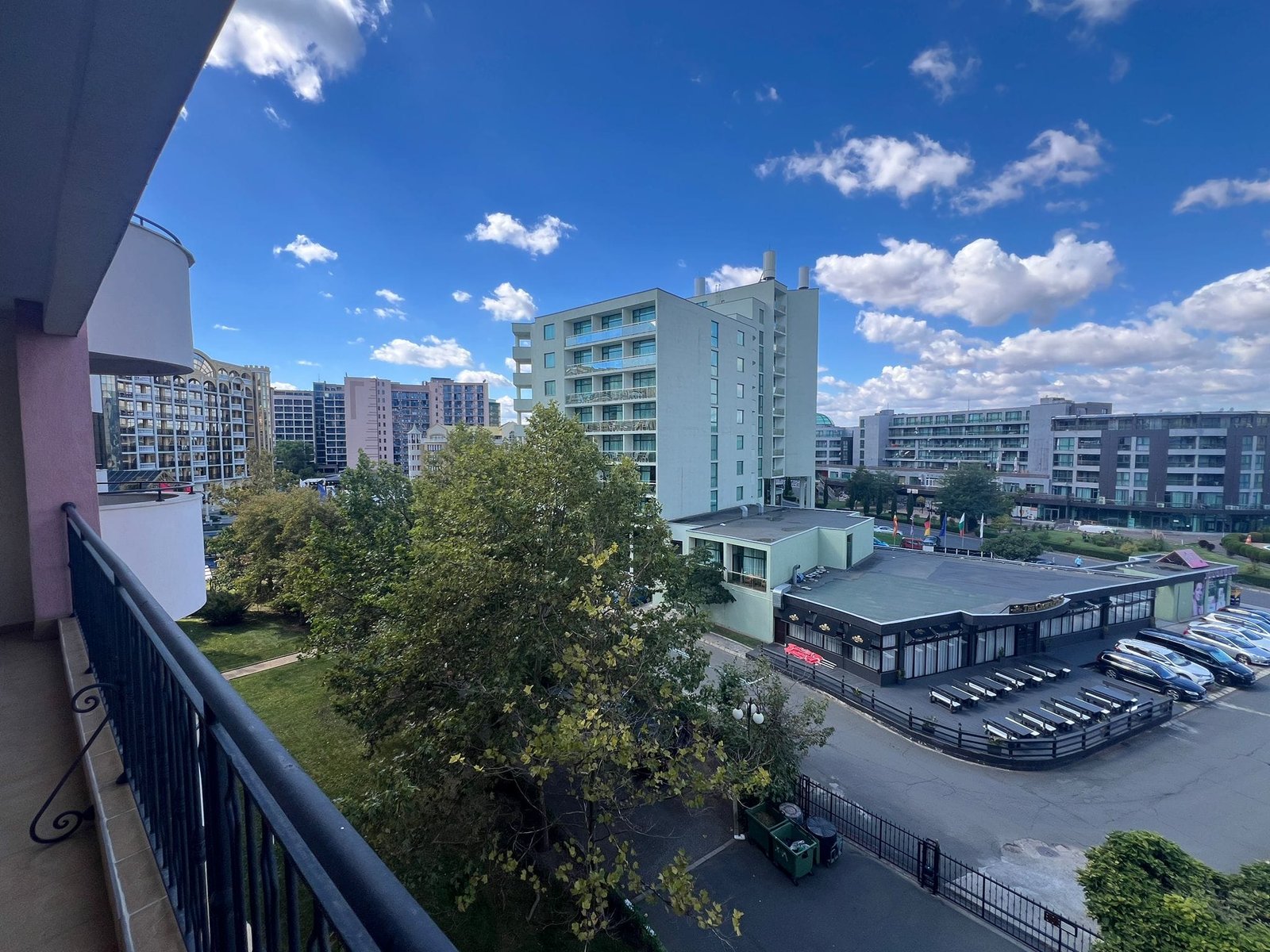 Современные здания и облачное небо в городе на фоне природы Балконный вид на жилые и коммерческие здания в Болгарии, зелёные насаждения и морская атмосфера. Продажа недвижимости.