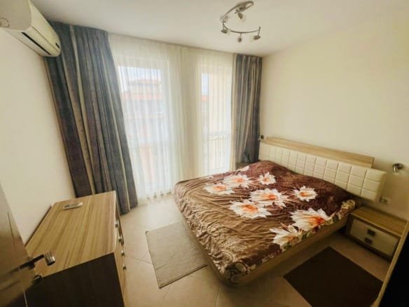 Уютная спальня с двуспальной кроватью, светлыми шторами и комодом, подходит для продажи недвижимости в Болгарии.