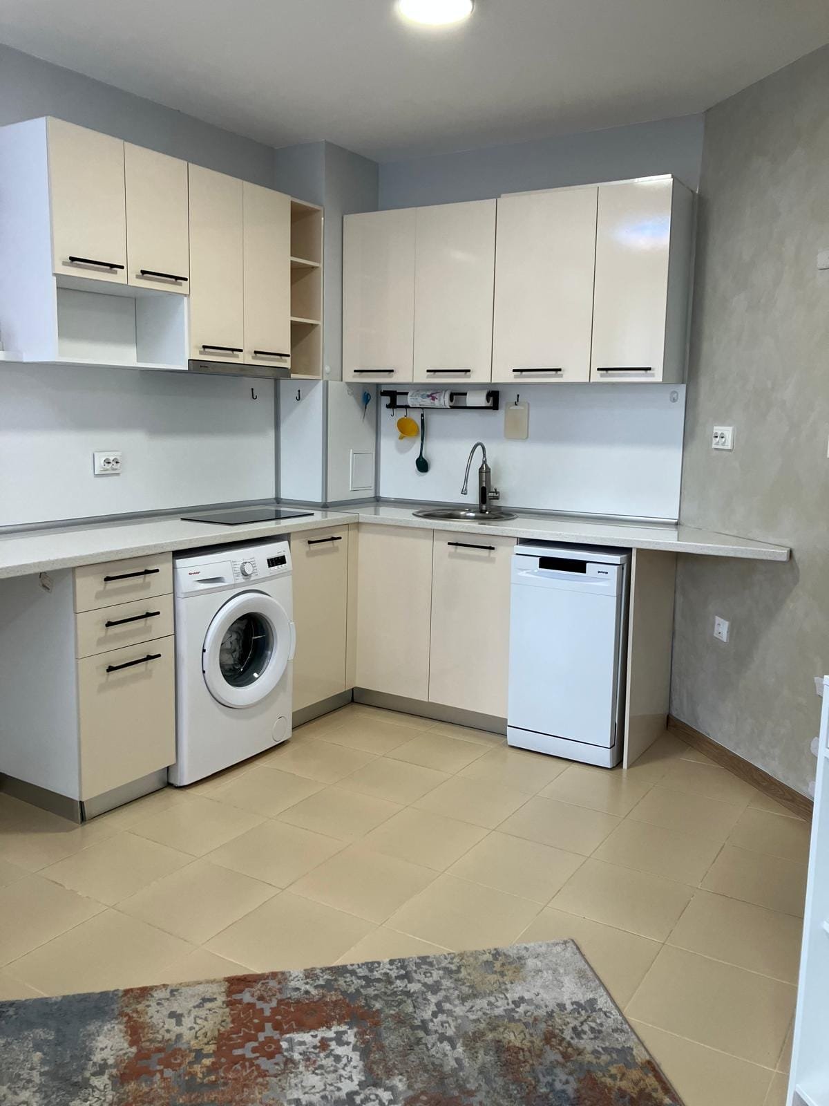 Современная кухня с бытовой техникой: стиральная машина, посудомоечная машина и светлые шкафы, подходящая для покупки недвижимости в Болгарии.