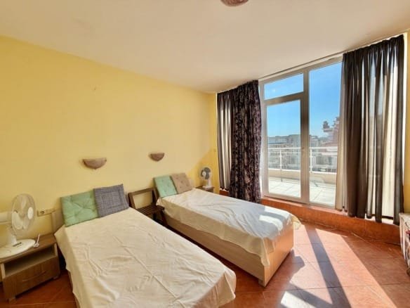 Светлая спальня с двумя раздельными кроватями, большими окнами и балконом, идеально подходит для аренды или покупки недвижимости в Болгарии.