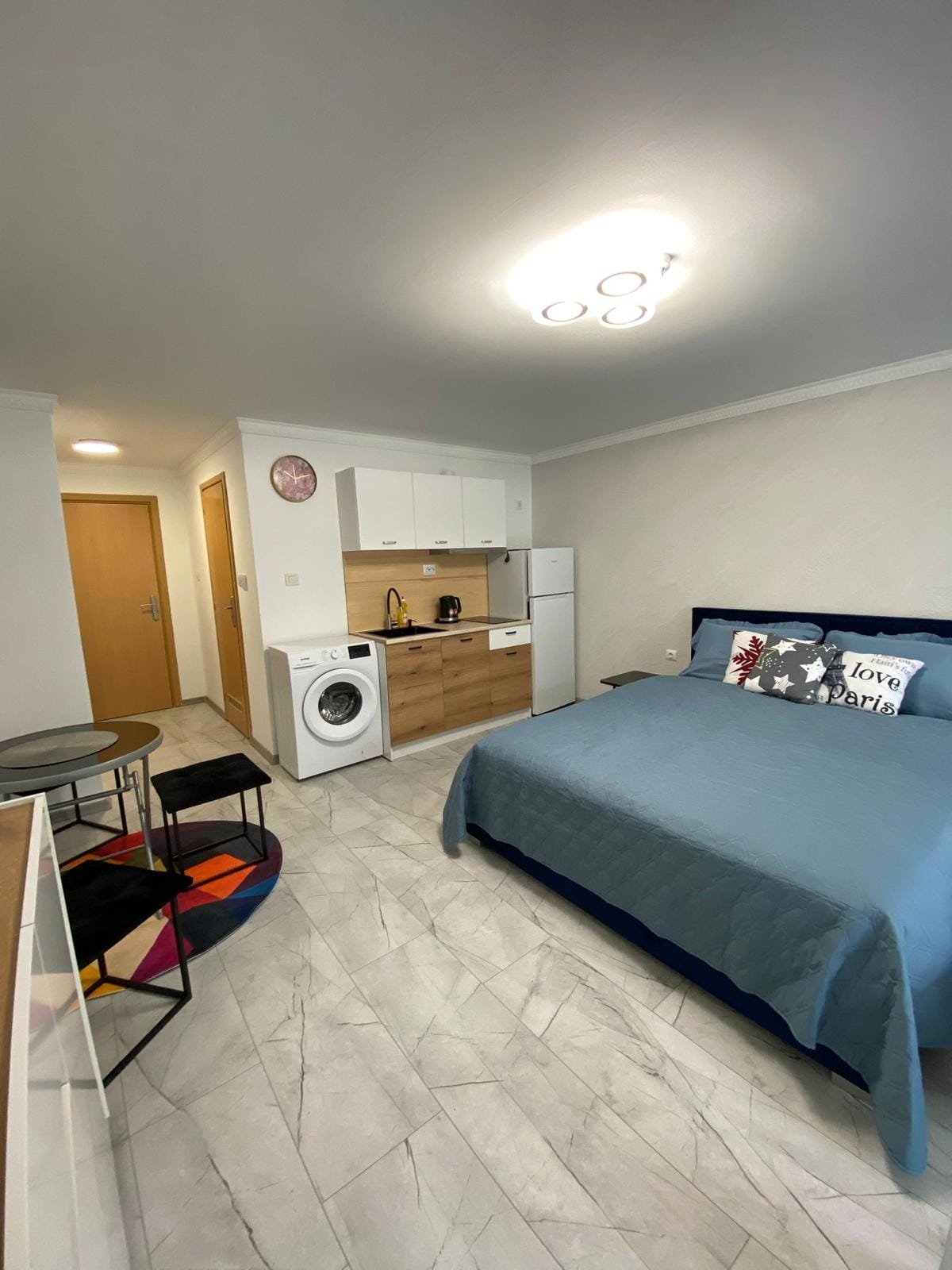 Современная квартира-студия с кухонной зоной, стиральной машиной и уютной спальней, подходящая для жизни в Болгарии.