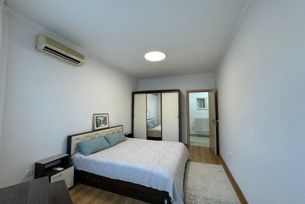 Современная спальня с двуспальной кроватью, светлыми стенами и зеркальным шкафом, идеально подходит для покупки недвижимости в Болгарии.