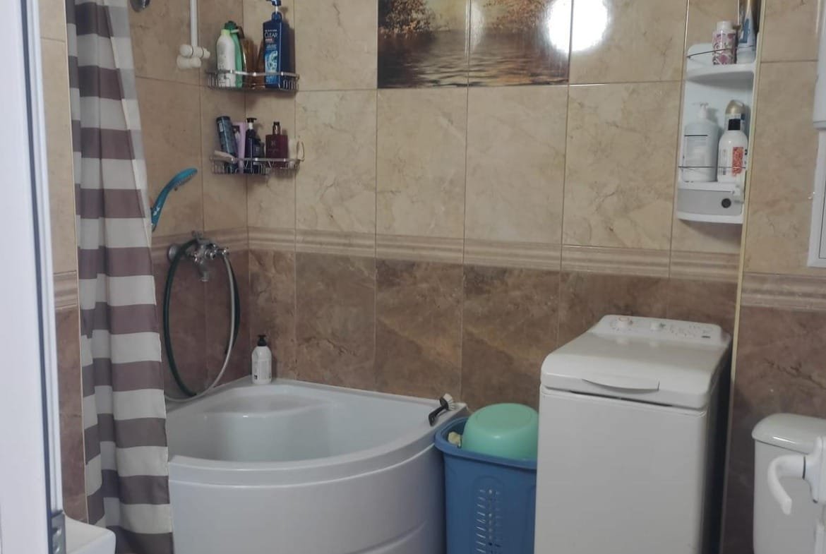 Светлая ванная комната с ванной, стиральной машиной и душем, отделанная плиткой, с элементами декора в виде картины.