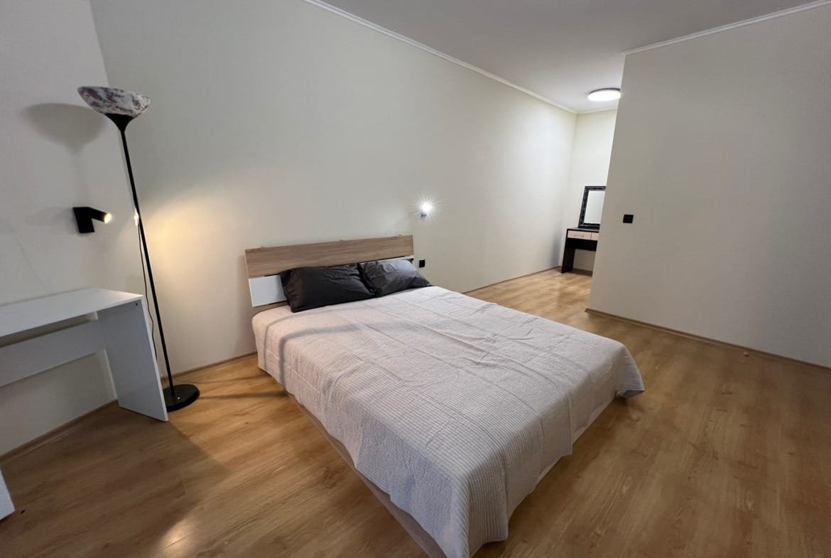 Современная спальня с лампой, двухспальной кроватью и светлым деревянным полом, подходящая для продажи недвижимости в Болгарии.