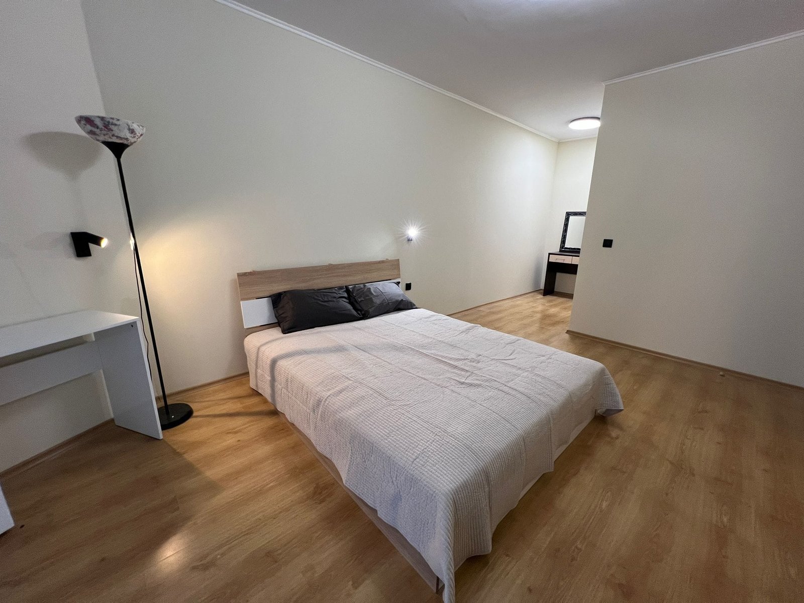 Современная спальня с деревянной кроватью и минималистичным дизайном Современная спальня с лампой, двухспальной кроватью и светлым деревянным полом, подходящая для продажи недвижимости в Болгарии.