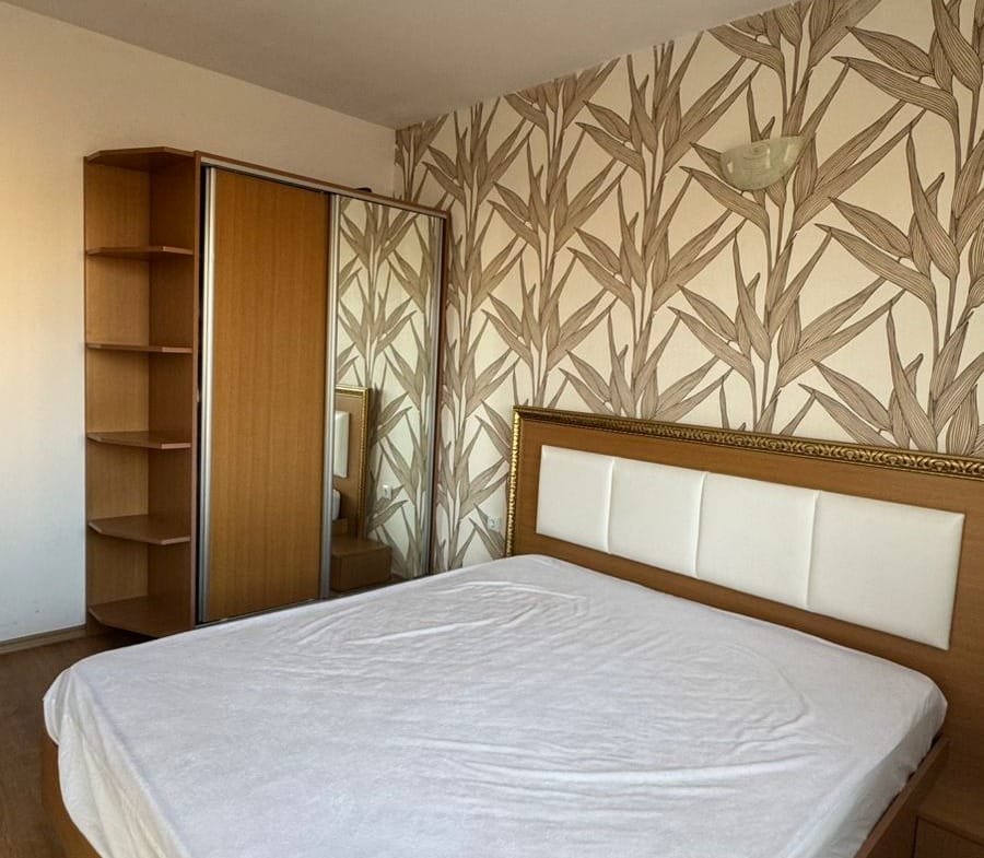 Красивая спальня с двуспальной кроватью, шкафом и оригинальными обоями в стиле природы, идеальная для покупки недвижимости в Болгарии.