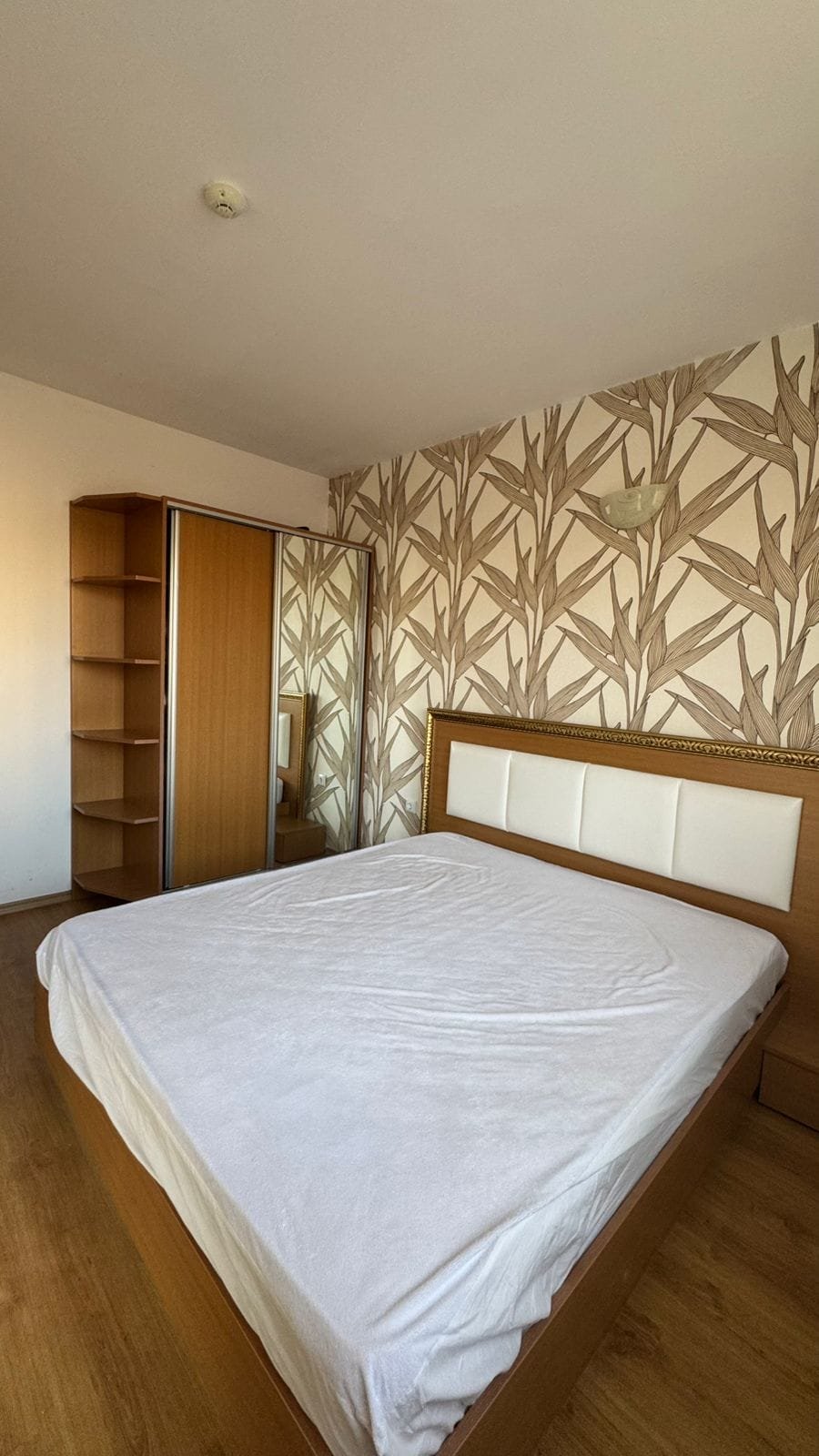 Красивая спальня с двуспальной кроватью, шкафом и оригинальными обоями в стиле природы, идеальная для покупки недвижимости в Болгарии.