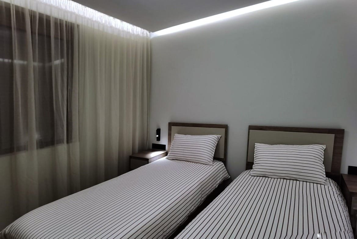 Современная спальня с двумя односпальными кроватями, светлым текстилем и мягким освещением, подходящая для жилья в Болгарии.