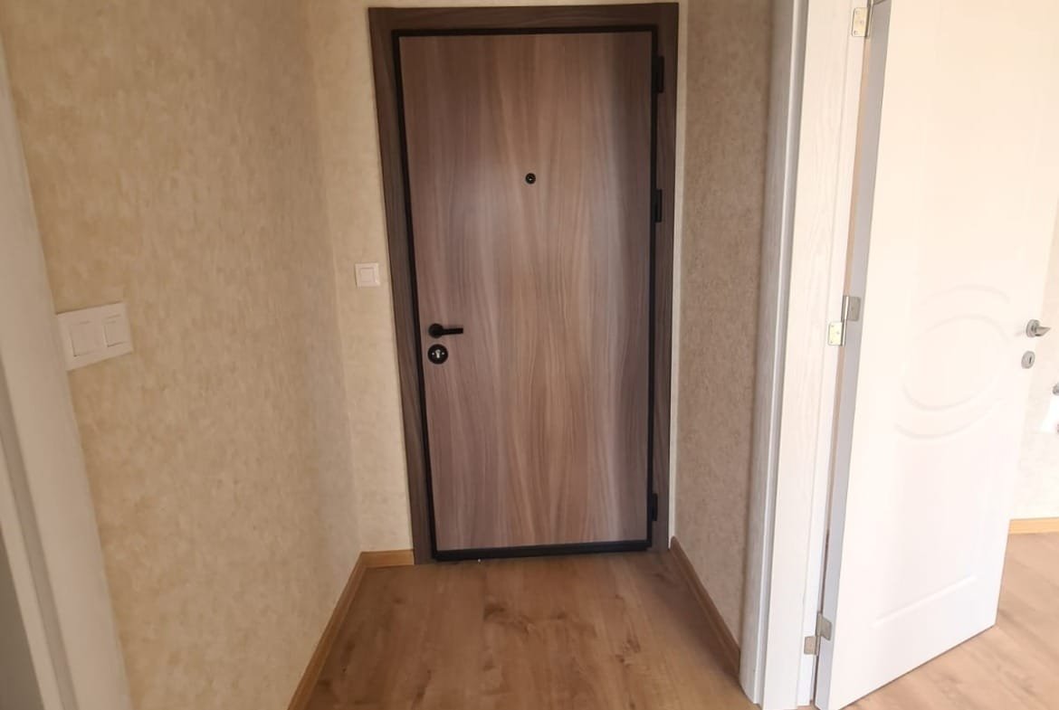 Современный вход в квартиру с деревянной дверью и светлыми стенами, пол из ламинированного покрытия, готов к продаже в Болгарии.