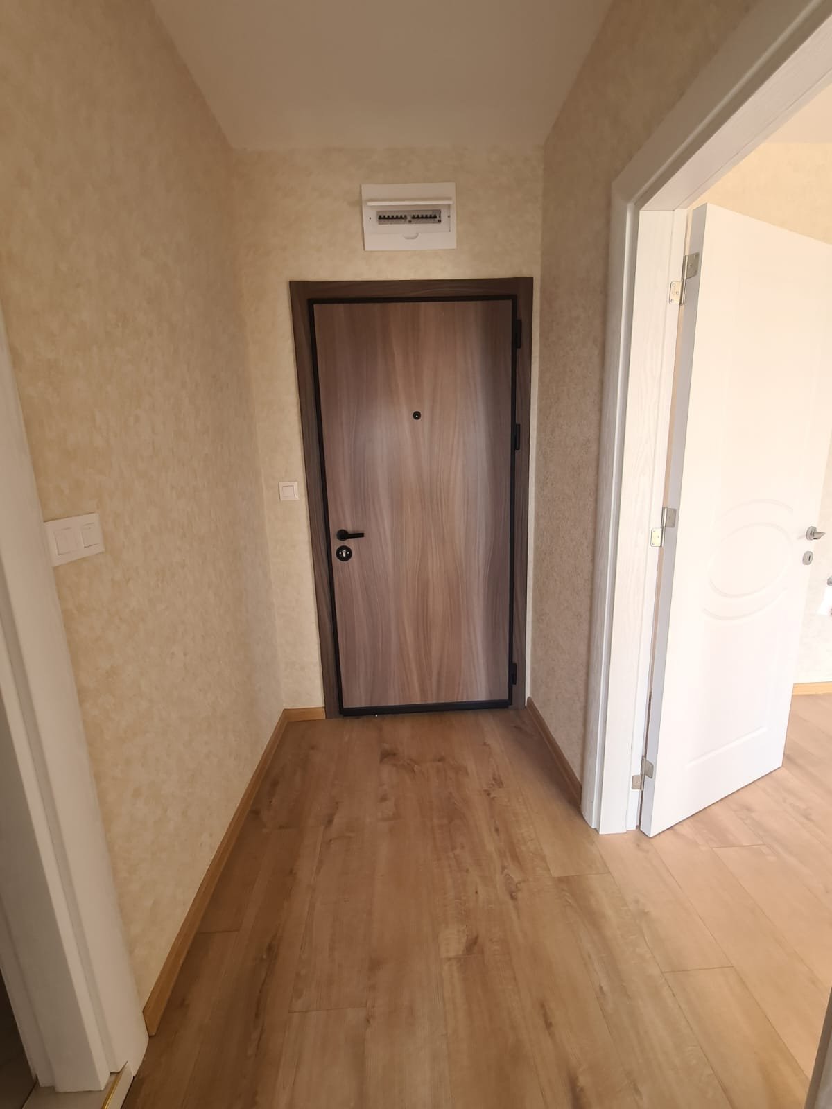 Современный вход в квартиру с деревянной дверью и светлыми стенами, пол из ламинированного покрытия, готов к продаже в Болгарии.