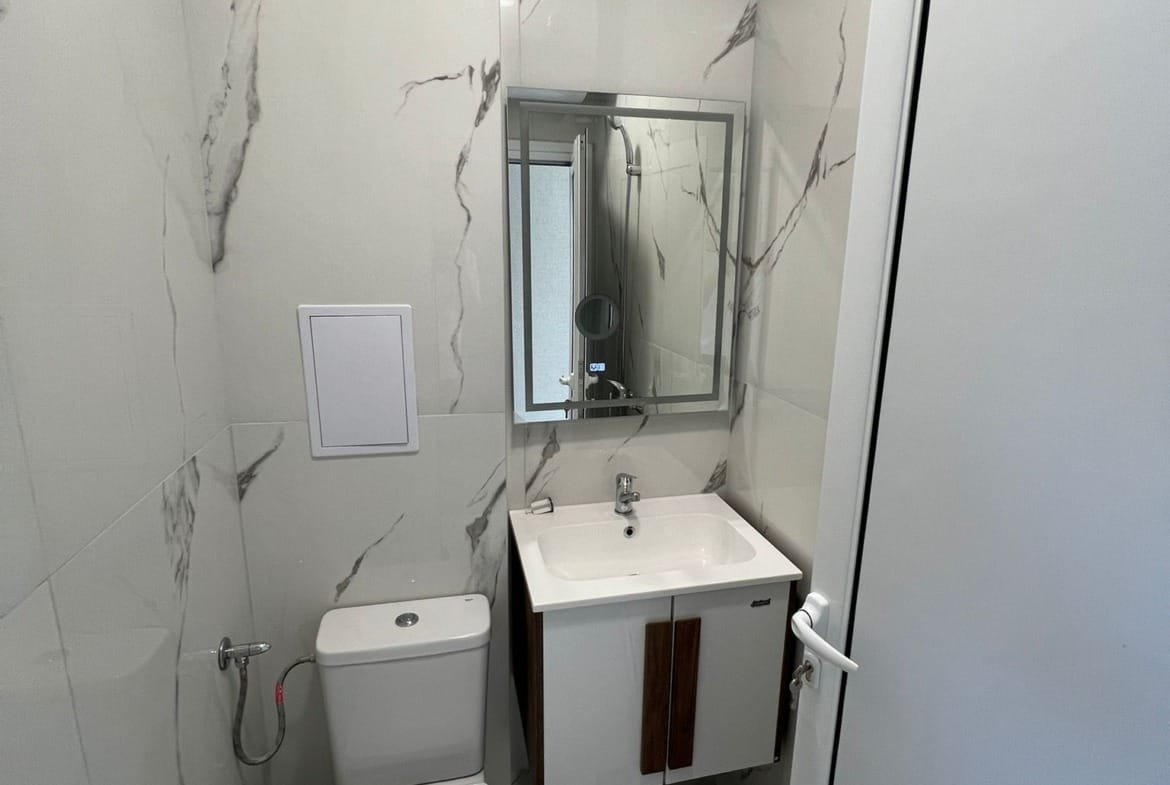 Современная ванная комната с мраморными стенами, белой сантехникой и зеркалом, идеально подходящая для покупки недвижимости в Болгарии.