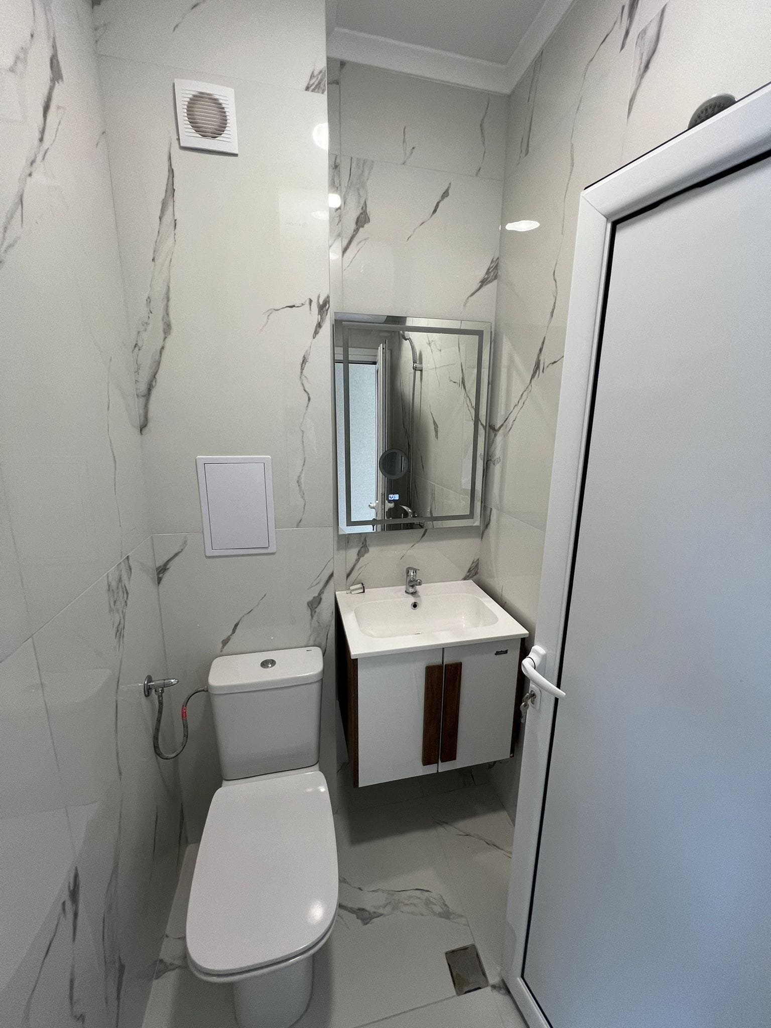 Современная ванная комната с мраморными стенами, белой сантехникой и зеркалом, идеально подходящая для покупки недвижимости в Болгарии.