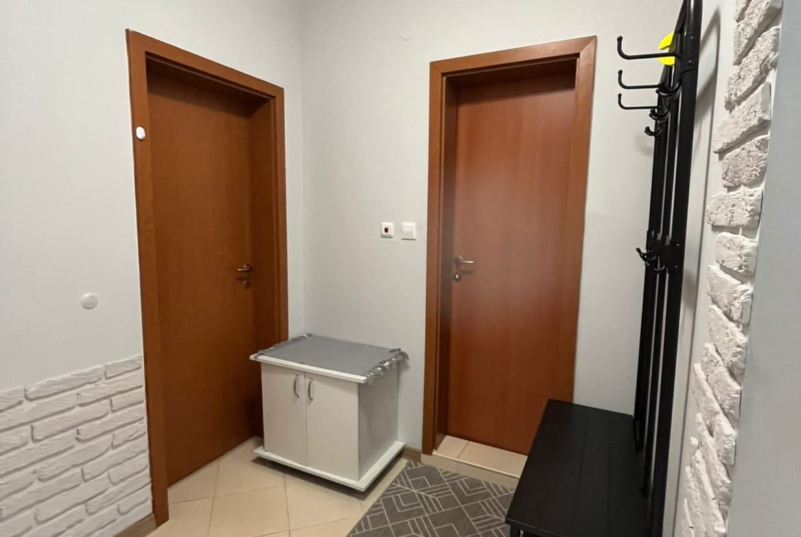 Современный коридор с двумя дверями, обувной тумбой и вешалкой, оформленный в светлых тонах, идеален для продажи недвижимости в Болгарии.