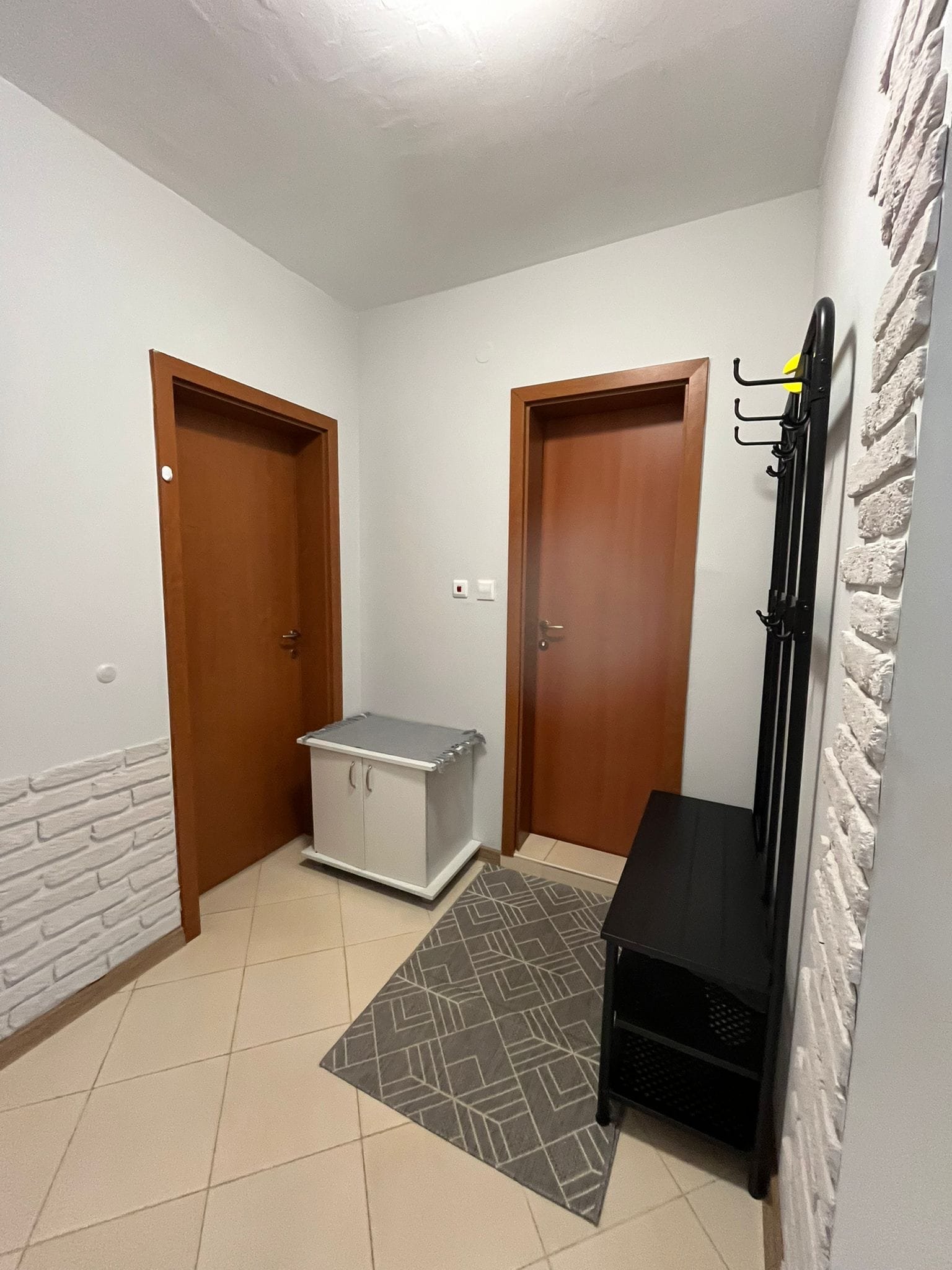 Современный коридор с двумя дверями, обувной тумбой и вешалкой, оформленный в светлых тонах, идеален для продажи недвижимости в Болгарии.