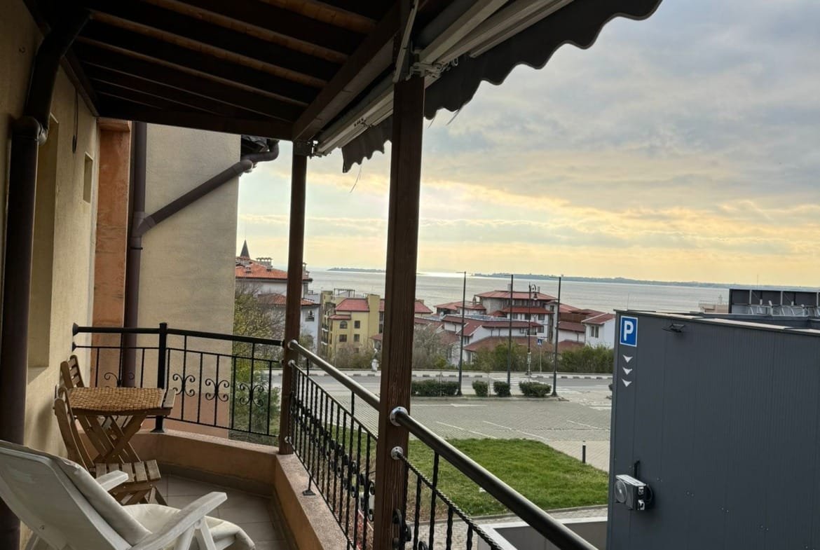 Балкон с лежаком и столиком, вид на море и жилые дома, идеальное место для отдыха в Болгарии.