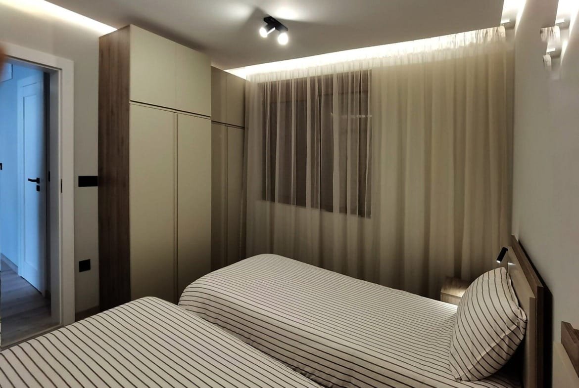 Современная спальня с двумя односпальными кроватями, светлыми стенами и гардеробной, подходит для покупки недвижимости в Болгарии.