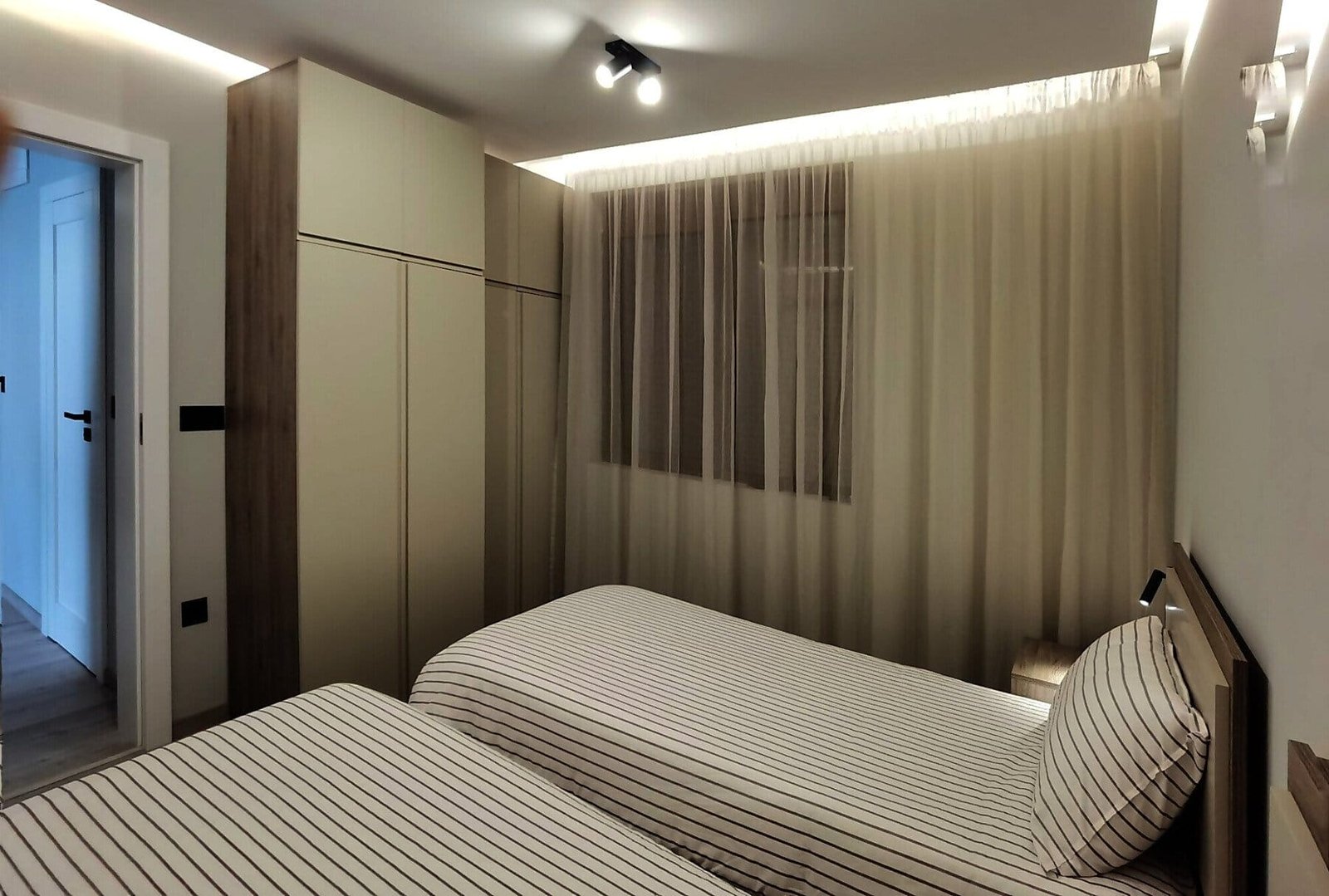 Современная спальня с двумя односпальными кроватями, светлыми стенами и гардеробной, подходит для покупки недвижимости в Болгарии.