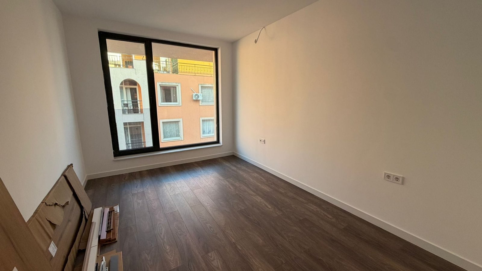 Пустая квартира с большим окном в современном жилом комплексе Светлая квартира с большими окнами и паркетным полом, готовая для покупки в Болгарии.