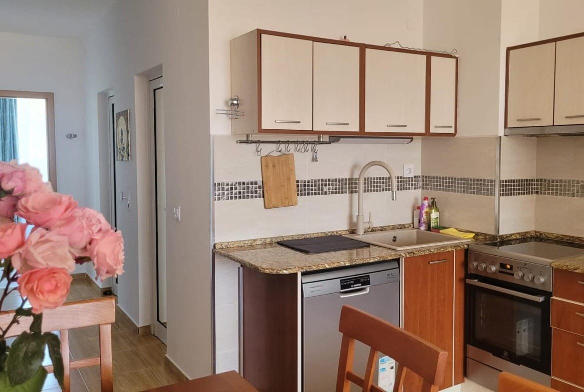 Современная кухня с гранитной столешницей, бытовой техникой и розами на столе, идеально подходящая для продажи недвижимости в Болгарии.