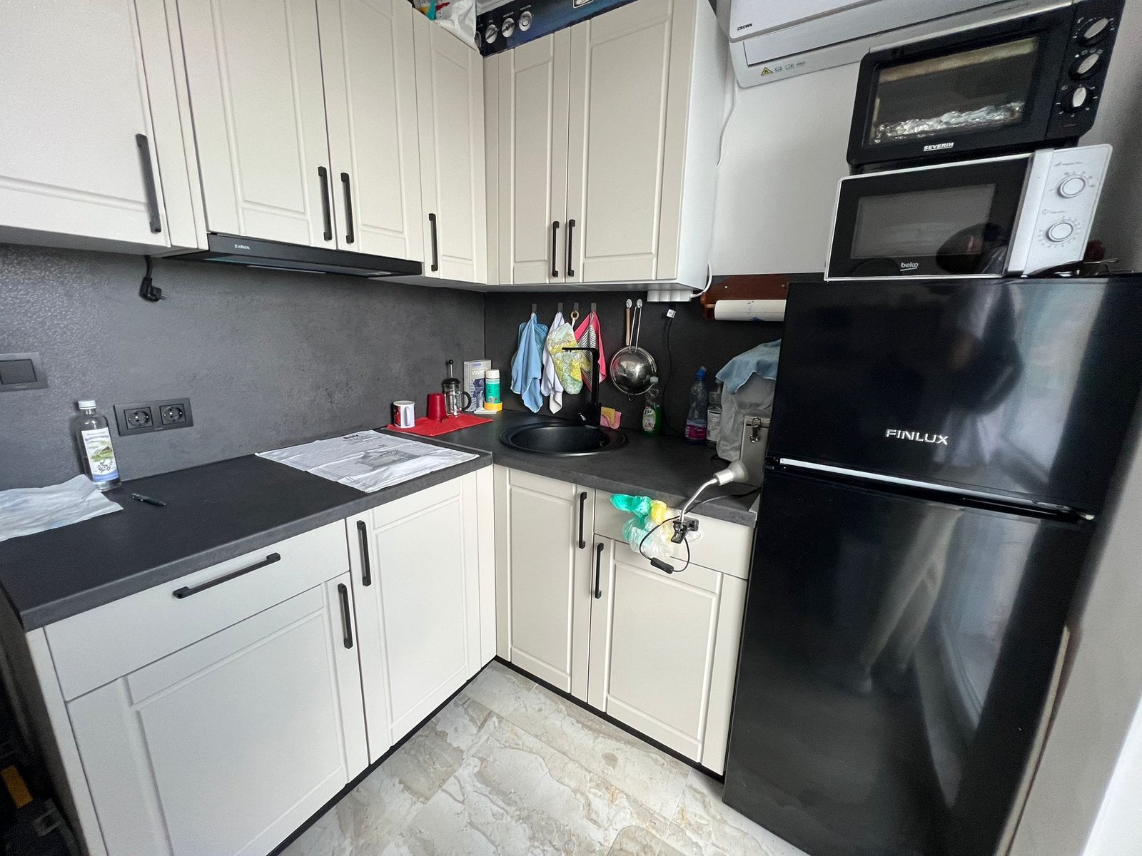 Современная кухня с черными бытовыми приборами, белыми шкафчиками и серой стеной, идеальна для покупки недвижимости в Болгарии.