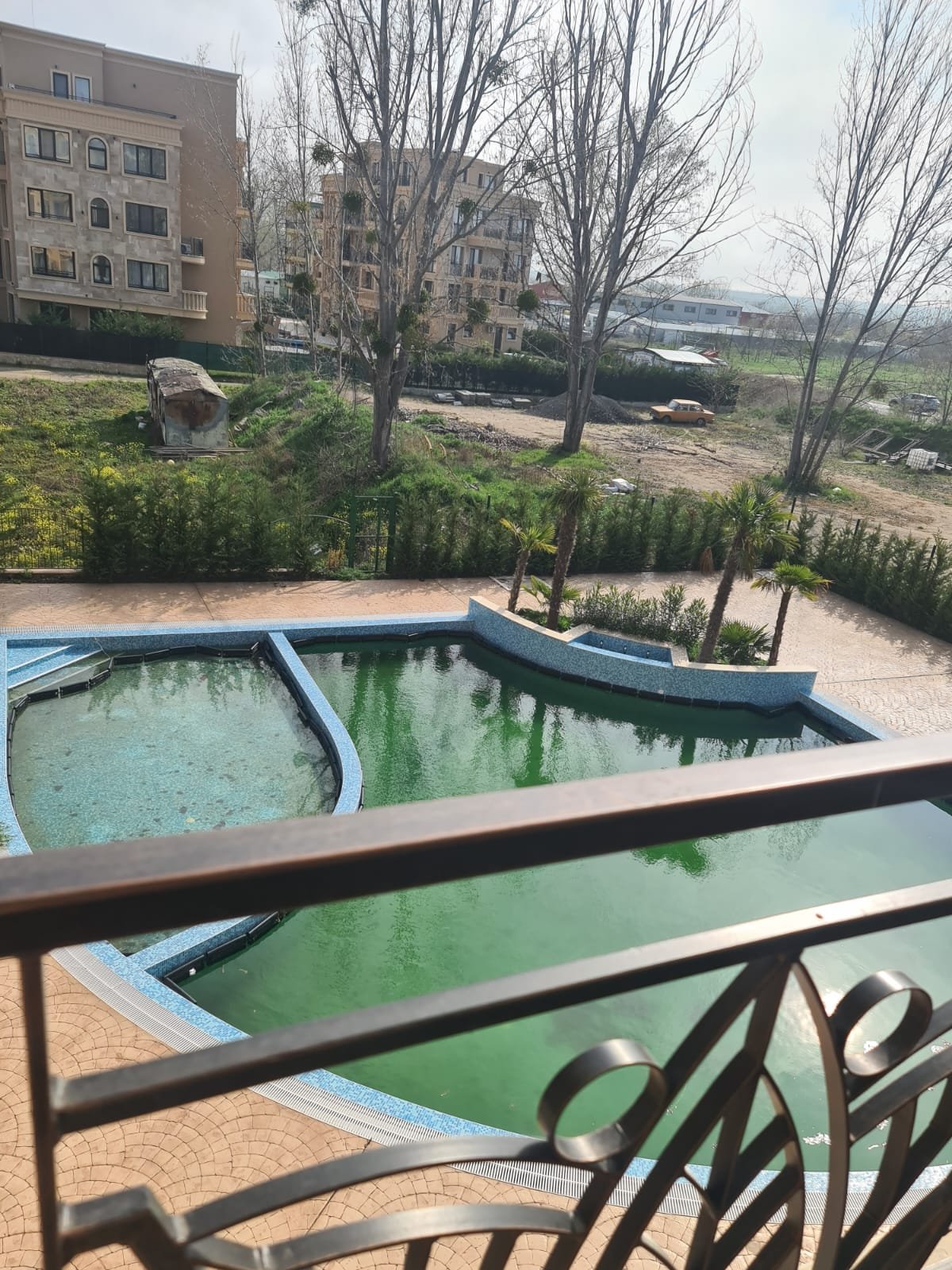 Панорамный вид на зеленоватый бассейн и окружающую территорию с новыми зданиями в Болгарии для продажи недвижимости.