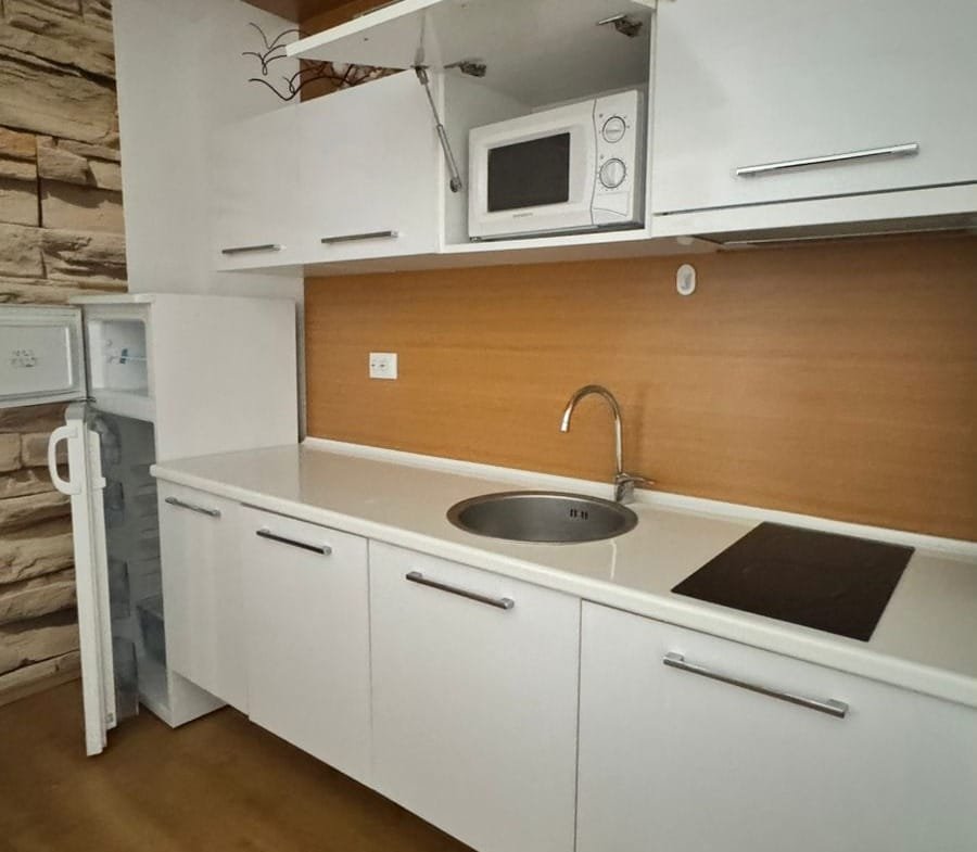 Современная кухня с белыми шкафами, встроенной мойкой и бытовой техникой, идеальная для покупки недвижимости в Болгарии.